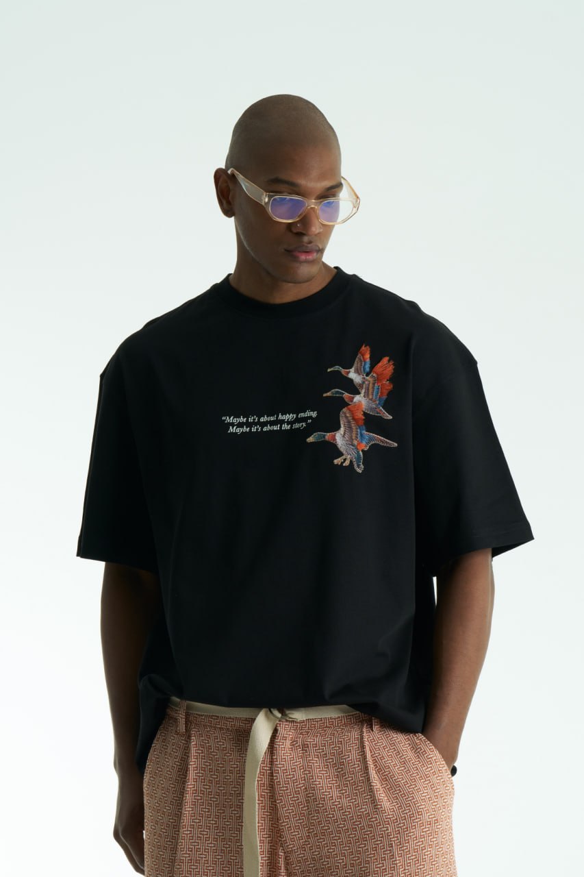 Black Oversized cotton T-shirt with embroidered flying ducks and quote print, shown in multiple colorways front and back.
