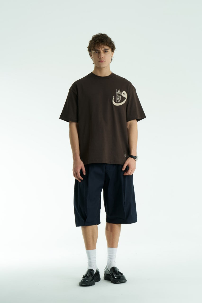 Brown Oversized cotton graphic T-shirt with small chest emblem and large ornate framed back print, shown in black, white, brown, and navy.