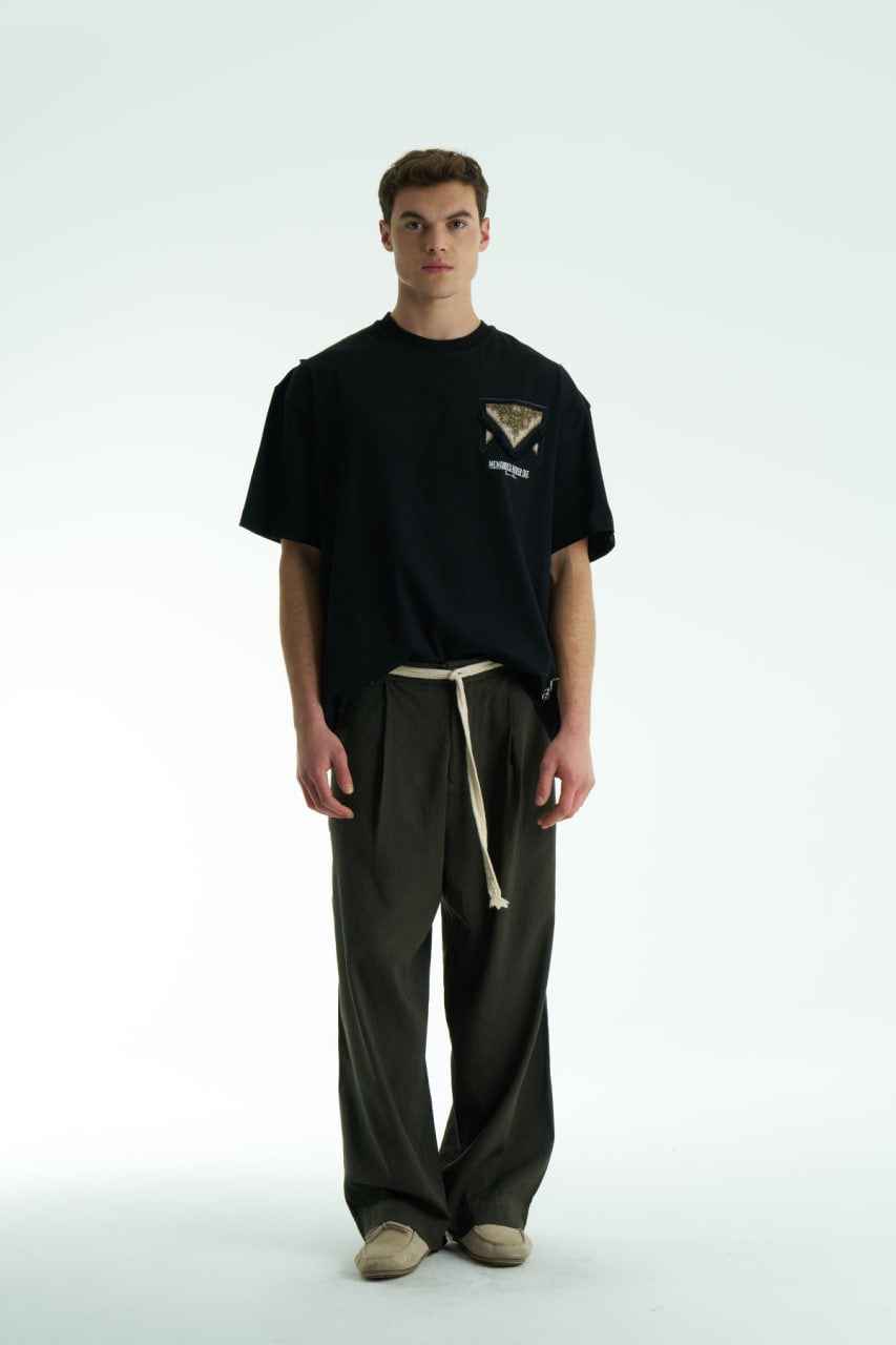 Black Oversized Memories Never Die cotton tee with chest pocket appliqué and scarf-style back yoke, shown in white, beige, and black.