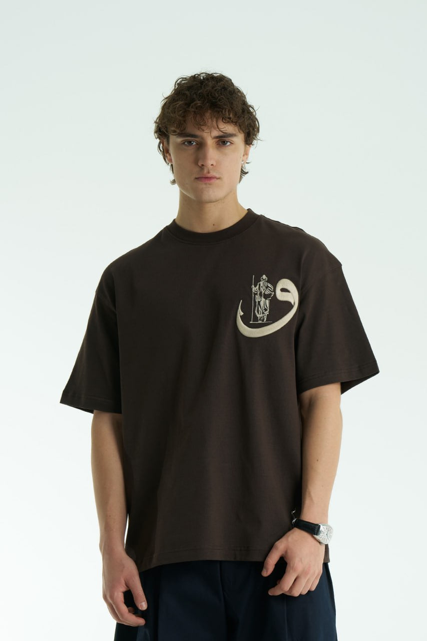 Brown Oversized cotton graphic T-shirt with small chest emblem and large ornate framed back print, shown in black, white, brown, and navy.
