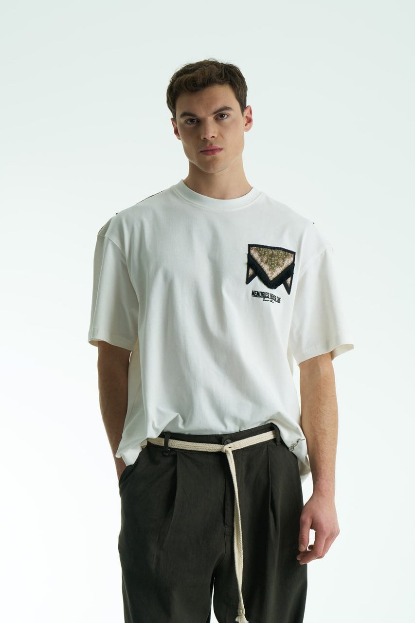 White Oversized Memories Never Die cotton tee with chest pocket appliqué and scarf-style back yoke, shown in white, beige, and black.