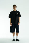 Black Oversized cotton graphic T-shirt with small chest emblem and large ornate framed back print, shown in black, white, brown, and navy.