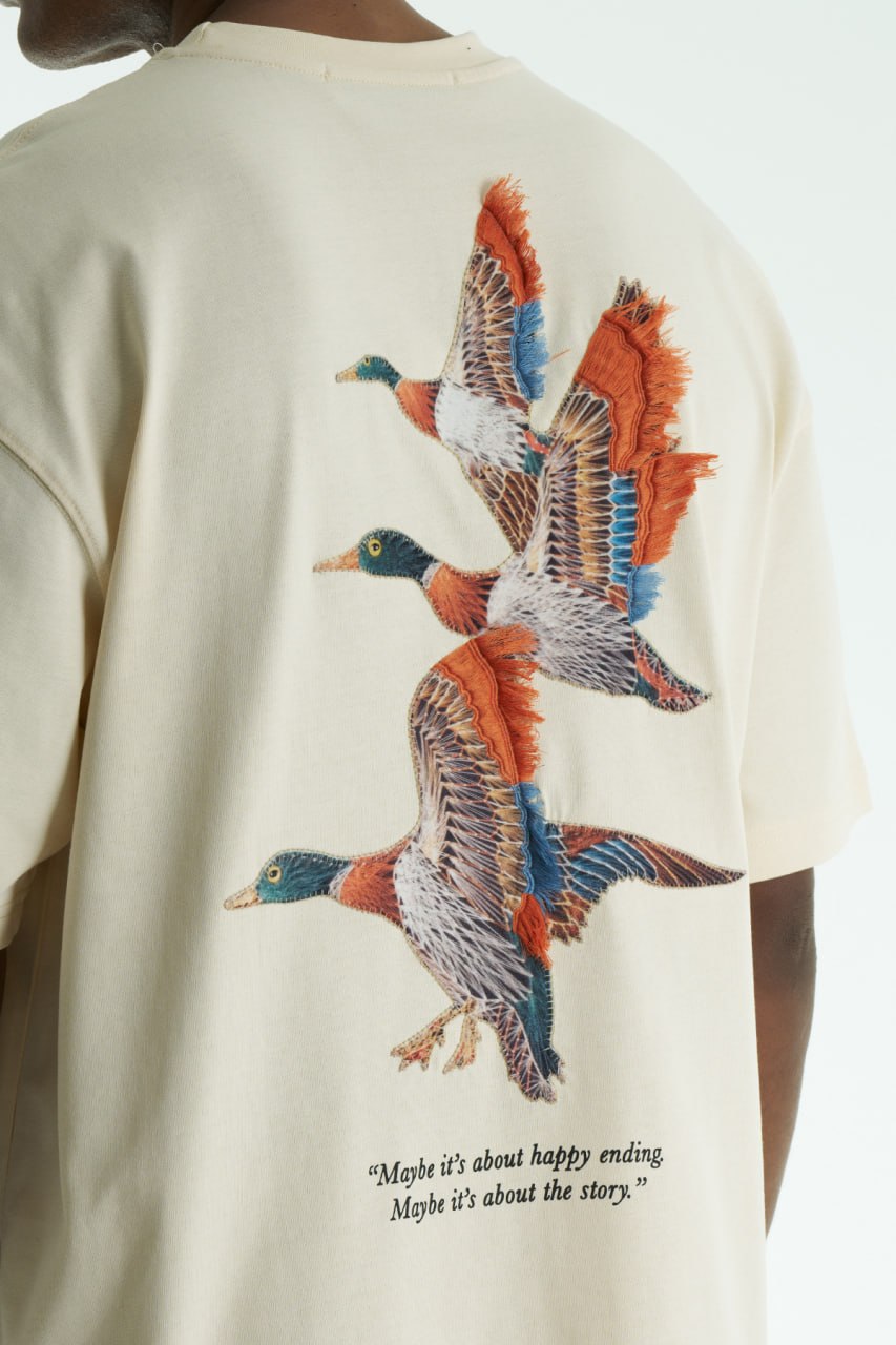 Beige Oversized cotton T-shirt with embroidered flying ducks and quote print, shown in multiple colorways front and back.